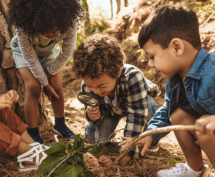 Kids exploring outdoors with magnifying glass.